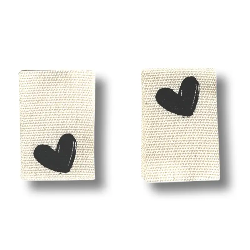 2 rechteckige Baumwoll-Labels mit schwarzen Herzaufdruck.